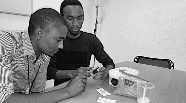 AREA lab technician Charles Bency Apollon (left) trains student intern Romial Louis how to use technologies — a DryCard and grain moisture hygrometer — to determine the moisture content of dry agricultural products.
